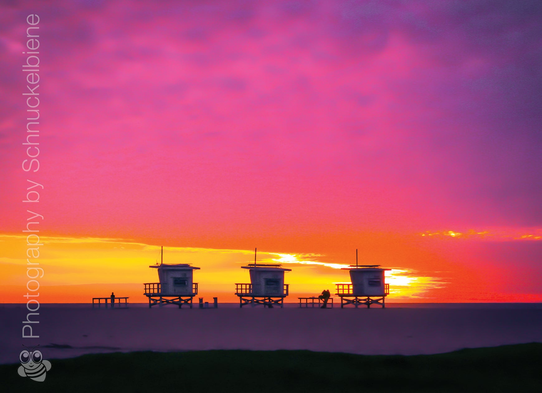 Three lifeguard towers on Santa Monica Beach under a pink and yellow winter sunset