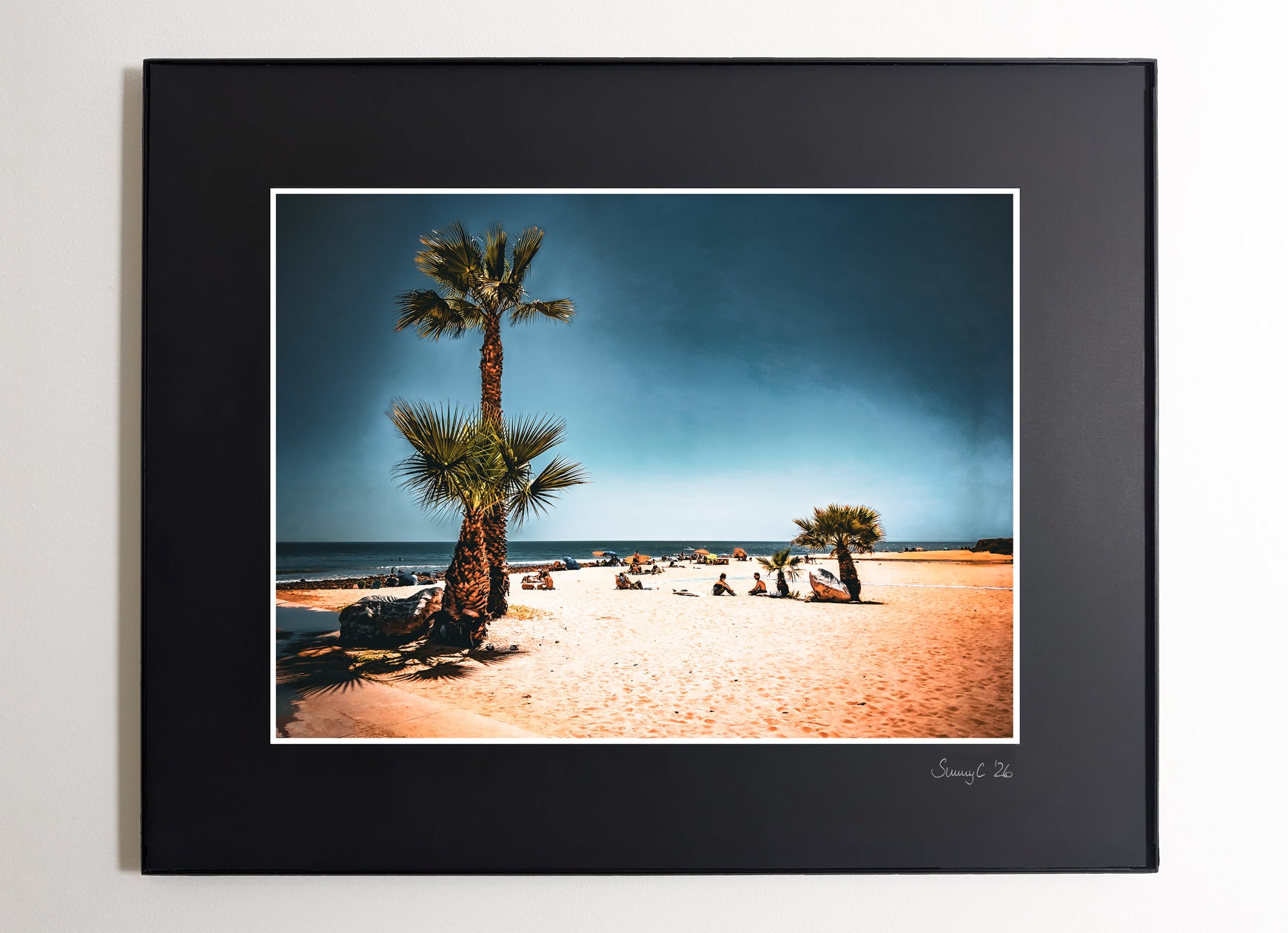 Framed photograph of a beach scene with palm trees and people sitting relaxed around