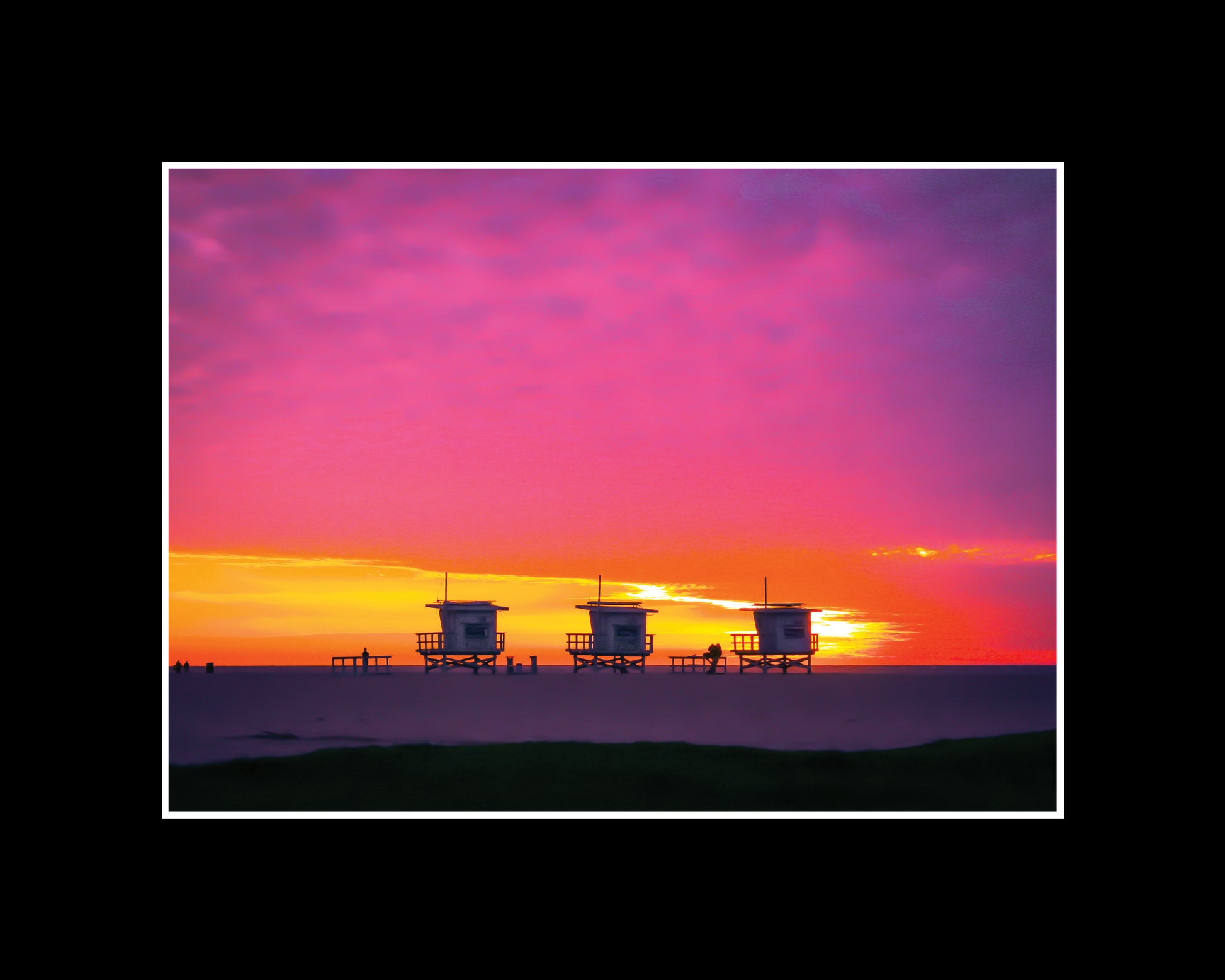 Three lifeguard towers on Santa Monica Beach under a pink and yellow winter sunset