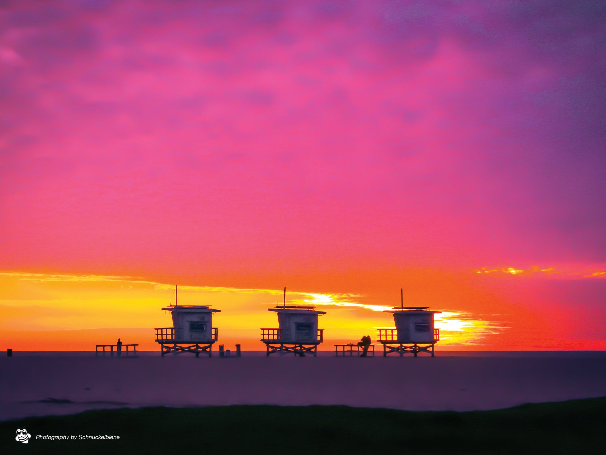 Three lifeguard towers on Santa Monica Beach under a pink and yellow winter sunset